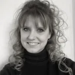 Black and white portrait of Shannon Seaver smiling, with curly hair styled in a high ponytail and bangs, wearing a dark turtleneck.